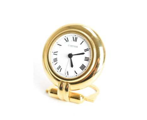 A Cartier travel alarm clock, having a circular brass case, white enamel dial with black Roman numerals, blue sapphire windin