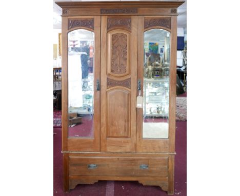 An Art Nouveau wardrobe, with central carved panel flanked by two mirrored cupboard doors with bevelled plates, raised on bra