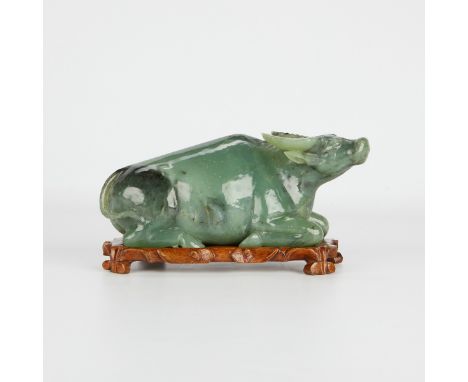 Chinese jade carving of an ox, of a dark celadon jade with darker inclusions. The carving rests on a wooden stand. With a cus