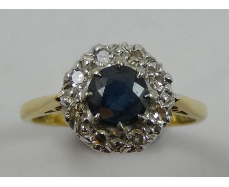 An 18ct gold sapphire and diamond cluster ring, claw set with a mixed cut stone, bordered by single cuts, size N.