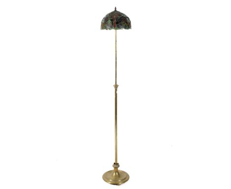 A Tiffany style shade mounted on a brass telescopic standard lamp base. The shade decorated with leaves and vines, the stand 