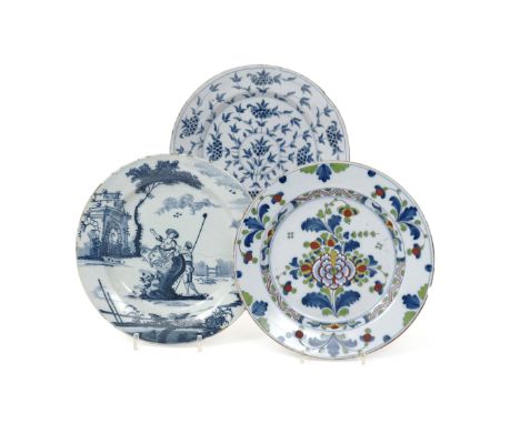 Three delftware plates  18th century, one painted with a shepherdess and shepherd beneath a tall tree beside Classical ruins,