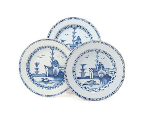 Three large delftware plates  mid 18th century, each painted in blue with a small building beneath tall stylized trees, the c