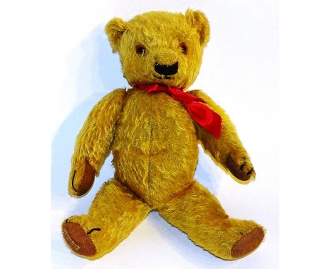 An early 20th century 'Chad Valley' plush teddy bear, wearing a red ribbon, sewn label to underside of right leg, 36cm high