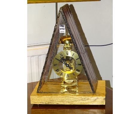 A modern skeleton mantel clock, within triangular glass cover, raised on oak plinth base, 40cm high