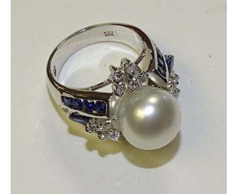 A 14ct white gold pearl, sapphire and diamond ring, the large central pearl flanked by 16 brilliant cut diamonds and a furthe