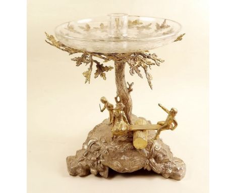 A large silver and silver gilt table centre piece in the form of an oak tree with children playing on a swing, with glass dis