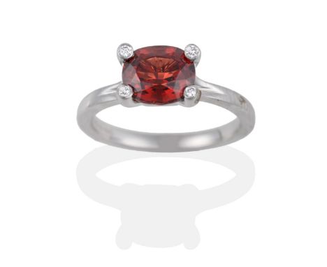 An 18 Carat White Gold Garnet and Diamond Ring, the oval mixed cut garnet in a four claw setting, each claw inset with a roun