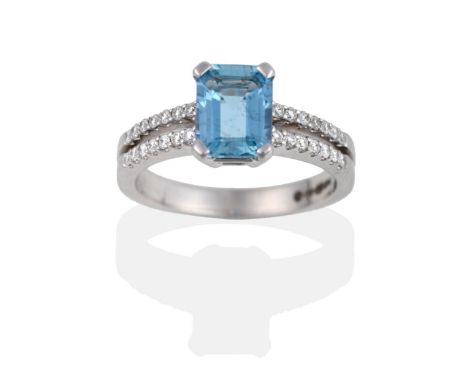 An 18 Carat White Gold Aquamarine and Diamond Ring, the emerald-cut aquamarine in a four claw setting to two row shoulders se