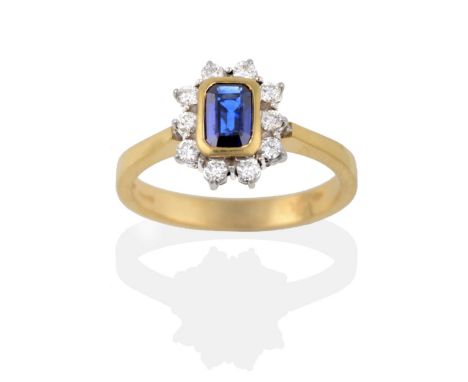 An 18 Carat Gold Sapphire and Diamond Cluster Ring, the emerald-cut sapphire in a yellow rubbed over setting within a border 