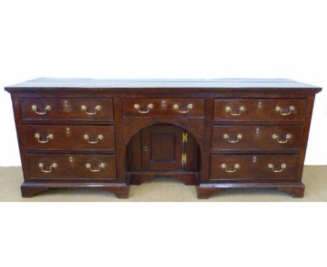 George III oak dresser base, two plank top above seven short drawers, arched centre recess with single panelled door, all sta