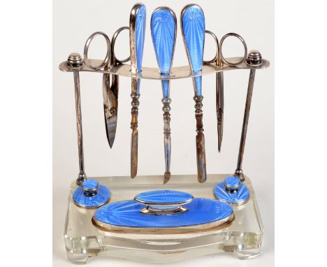  An eight piece manicure set with silver and blue guilloche enamel handles, on a silver and glass display stand, by Walker & 