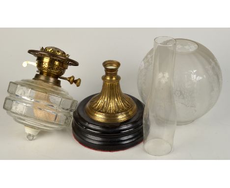 An oil lamp with a glass reservoir on a brass and black glass base and etched shade.
