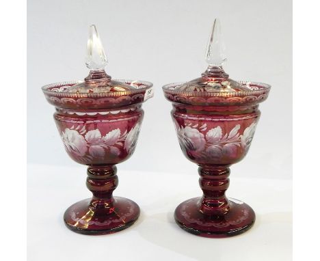 Pair of Victorian cranberry glass pedestal lidded urns with clear glass finials, rose etched decoration, on circular pedestal