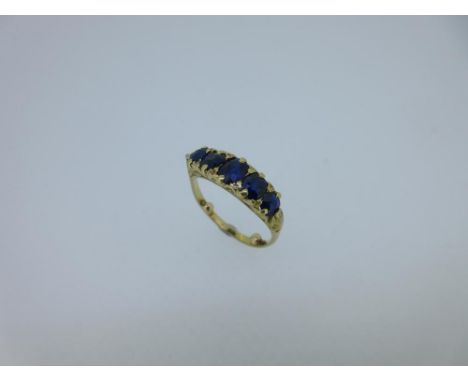 A five stone sapphire ring, the graduated line of oval cut sapphires close claw set to a carved scrolling gallery and shoulde