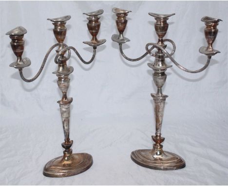 A pair of silver-plated three-light candelabra/ converting to candlesticks, of plain oval section with bands of horizontal re