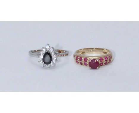 A 14k gold ring, centrally four claw set with a solitaire ruby coloured stone flanked by six smaller ruby coloured stones to 