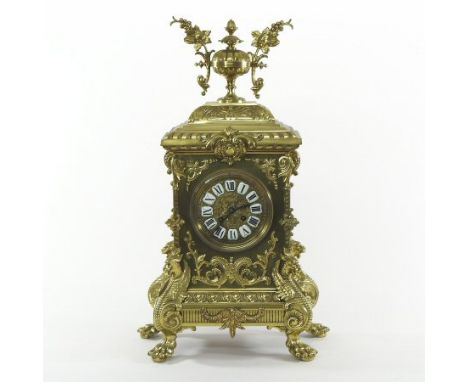 An ornate 19th century continental brass cased mantel clock, surmounted by an urn, decorated with scrolls and dragons, on paw