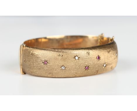 A 9ct gold, diamond and synthetic ruby oval hinged bangle, the front mounted with circular cut diamonds and synthetic rubies 