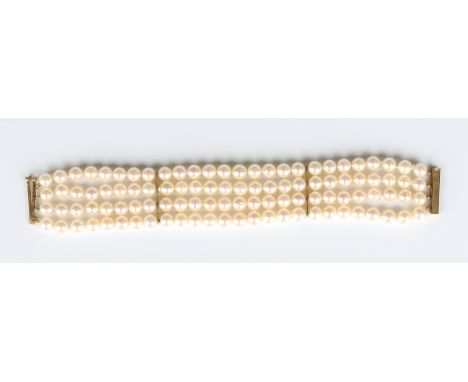 A four row bracelet of uniform cultured pearls on a gold sliding clasp with engine turned decoration, detailed '750', length 