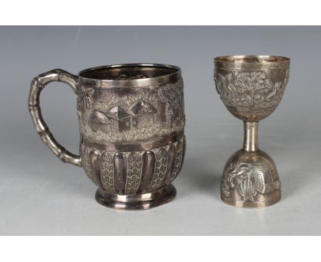 A late 19th/early 20th century Indian silver tankard, the body chased with figures in village scenes, flanked by simulated ba