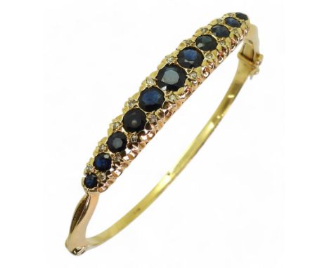 A SAPPHIRE &amp; DIAMOND BANGLE made in 18ct gold hallmarked London 1975. The scalloped galleried mount is set with round cut