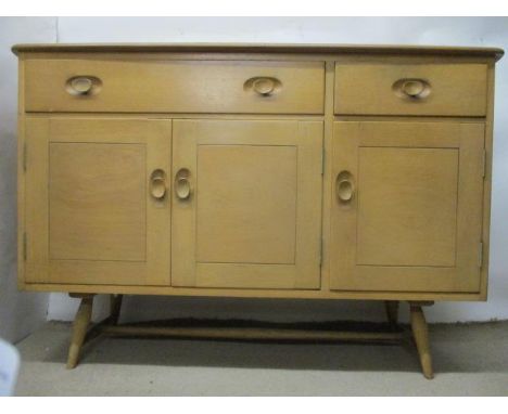 A mid 20th century Ercol Windsor light elm sideboard with a long and a short drawer over three doors, raised on turned, splay