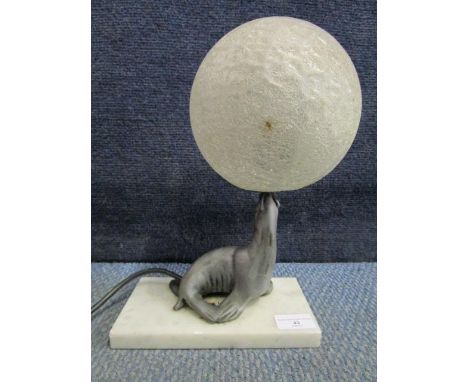 An Art Deco style table lamp in the form of a seal, mounted on a white marble base, balancing a frosted and ice glass globe s