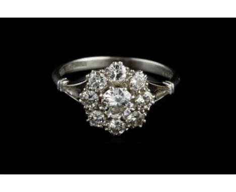 A DIAMOND FLOWERHEAD CLUSTER RING, the graduated round brilliant-cut diamonds in claw setting, between openwork fleur-de-lys 