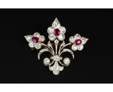 A RUBY AND DIAMOND FLORAL SPRAY BROOCH, the fleur-de-lys shaped panel issuing a trio of flowerhead clusters, each centred wit