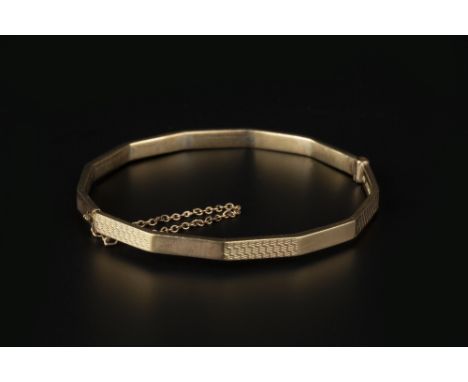 A PANELLED BANGLE, of hinged oval form, with alternate polished and engine-turned panels, stamped '9ct', inner diameter 6cm