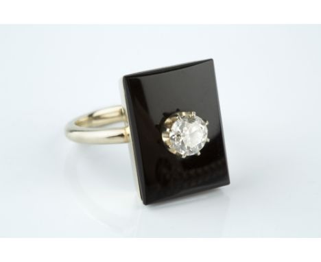 A DIAMOND AND ONYX PANEL RING, the rectangular onyx panel centred with a round brilliant-cut diamond in claw setting, indisti