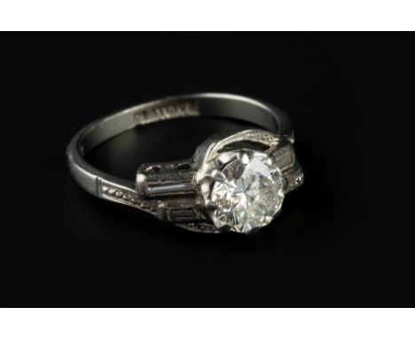 A DIAMOND SINGLE STONE RING, the principal round brilliant-cut diamond in claw setting, to a crossover setting with baguette-