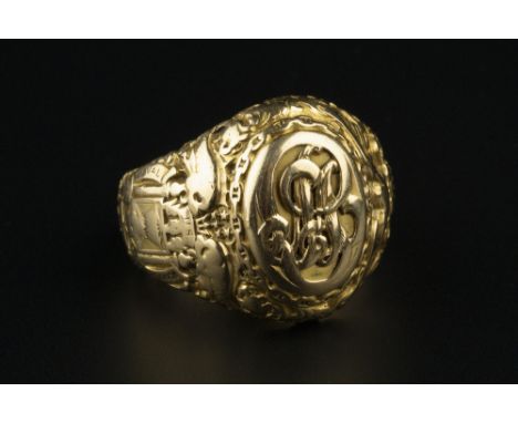 A YELLOW PRECIOUS METAL SIGNET RING, the oval panel applied with a scrolled monogram, between tapered profusely decorated sho