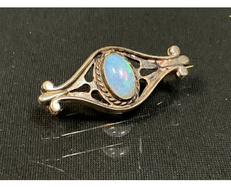 An Arts &amp; Craft oval opal cabochon inset shaped brooch, unmarked silver coloured metal mount, the opal with strong green.