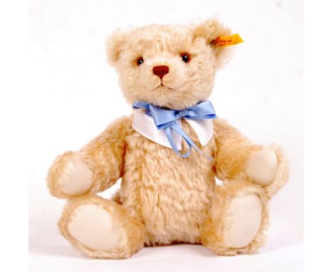 A contemporary Steiff blonde mohair teddy bear. Glass eyes, with blue bow tie. Steiff tag to ear ' Steiff 654510 '. With tags