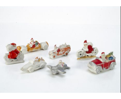 Seven unusual bisque Father Christmas cake decorations in vehicles,  including one driving a wheeled Christmas cracker --4in.