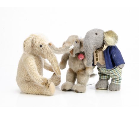  Two artist made elephants, a grey plush jointed elephant with checked trousers and blue jacket --11 ½in. (29.5cm.) high; a c