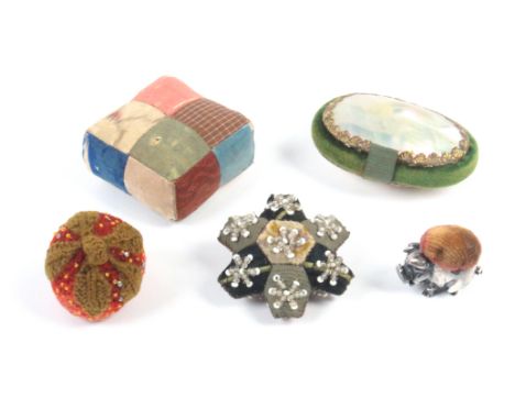 Five pincushions and emeries comprising a knitted and beaded strawberry, a silk patchwork example, a geometric beaded patchwo