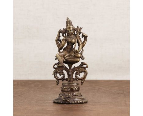 A bronze bodhisattva, 20th century, possibly Indian, seated on a tall lotus pedestal, each of her two pairs of hands holding 