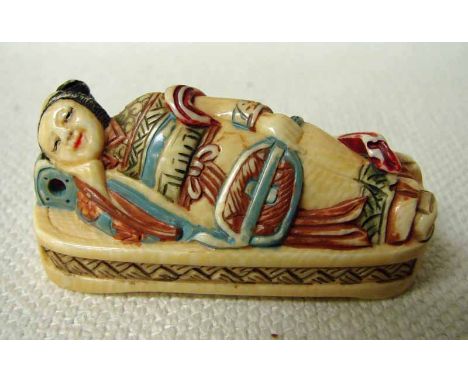 An early 20th century Japanese ivory Netsuke, a robed lady holding a fan, asleep on a bed, signed to underside, 5cm long