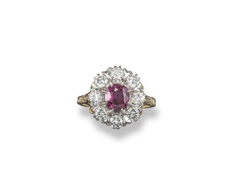 A ruby and diamond cluster ring, the oval-shaped ruby is set within a surround of circular-cut diamonds in platinum and yello