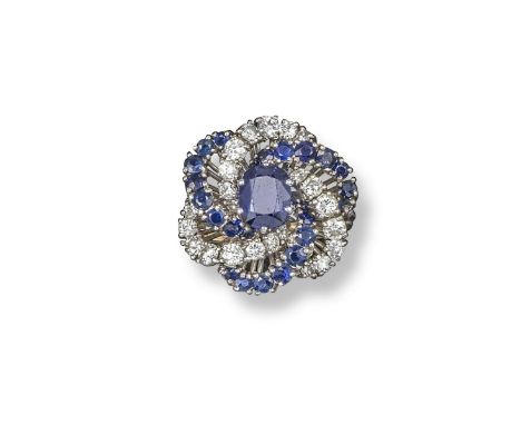 A sapphire and diamond cluster ring, set with a central cushion-shaped sapphire within scrolling lines of sapphires and diamo