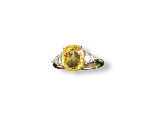 A sapphire and diamond ring, the oval-shaped yellow sapphire is set with a tapered baguette and triangular diamond to each sh