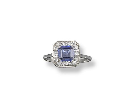 A sapphire and diamond cluster ring, the square shaped sapphire is millegrain-set within a surround of circular-cut diamonds 