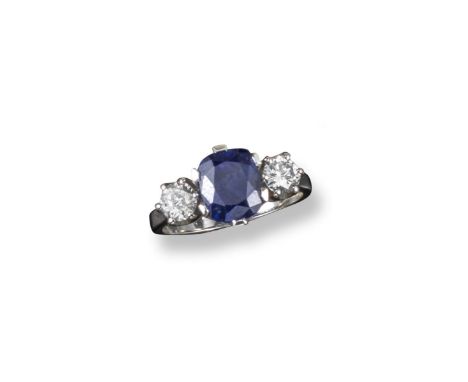 A sapphire and diamond three stone ring, the cushion-shaped sapphire is set between two circular-cut diamonds in platinum. Si