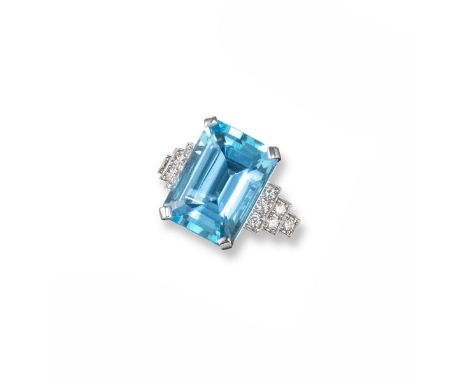 A large blue topaz and diamond set ring, the emerald cut topaz is millegrain set with six circular cut diamonds to each shoul