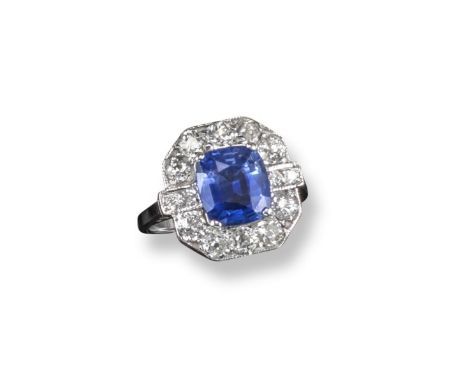 A sapphire and diamond ring, the cushion-shaped sapphire is set within a surround of old circular-cut diamonds in white gold.