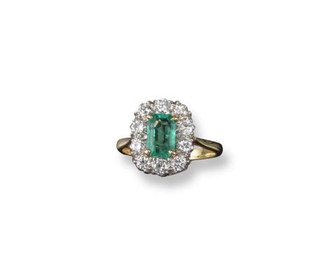 An emerald and diamond cluster ring, the emerald-cut emerald is set within a surround of circular-cut diamonds in platinum an