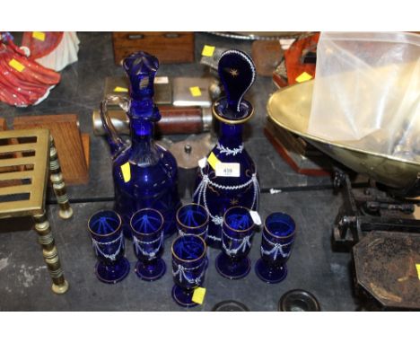 A early 20th century blue glass decanter and 6 glasses decorated in white and guilt with swags and ribbons and sold with a co